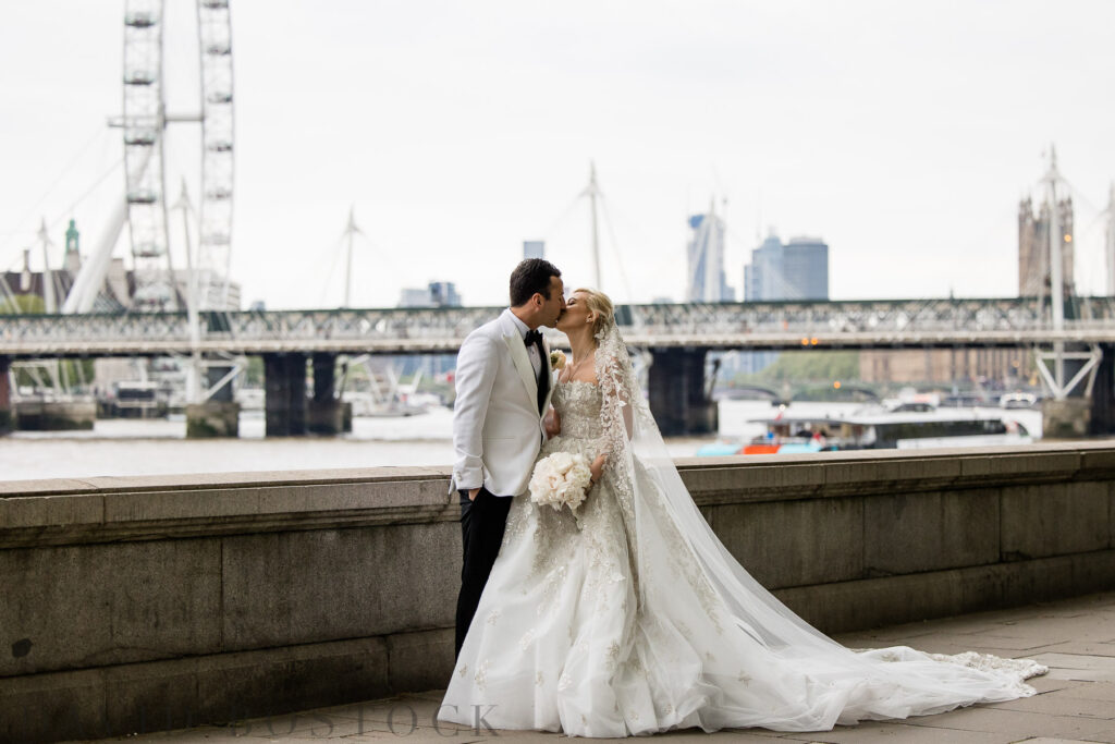 bride and groom kissing in front of river thames