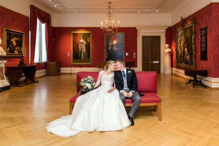 bride and groom sitting on a bench in one of the Ashmolean Museum galleries looking at each other