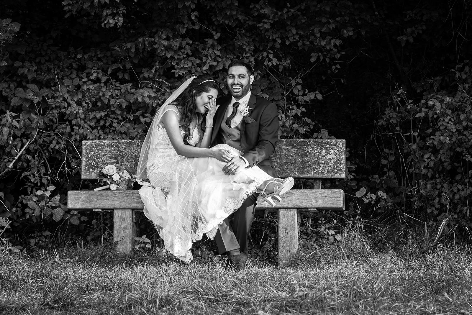 Indian bride and groom sitting on a park bench laughing together