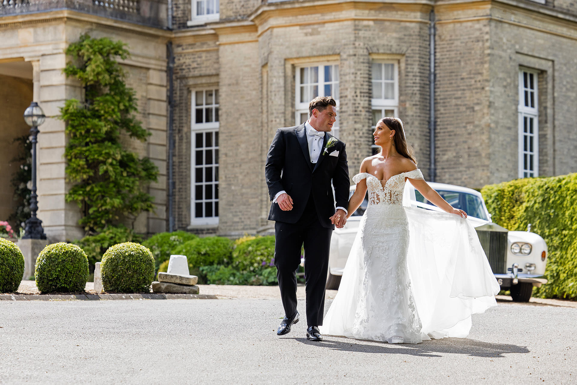 Bride and groom walking hand in hand down the driveway at Hedsor House with a Rolls Royce in the background